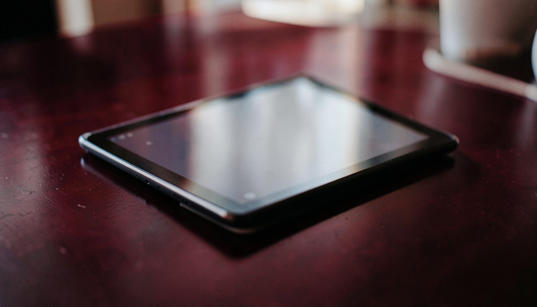 A close-up documentary photograph of a sleek digital tablet resting on a dark polished tabletop, with soft maroon reflections and a calm, professional ambiance.